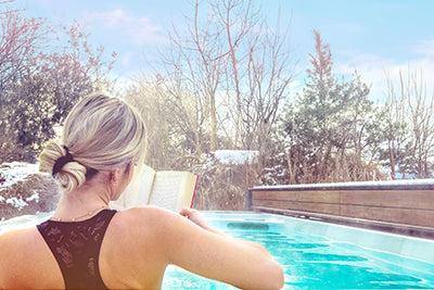 Eine junge Frau sitzt an einem kalten Wintertag in einem beheizten Swimmingpool und liest ein Buch vor ihrem Schwimmtraining mit der kraftvollen Gegenstromanlage.