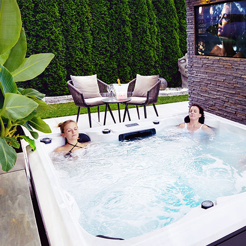 Zwei Frauen entspannen sich in einem Infinity Whirlpool neben dem Haus auf der Terrasse.