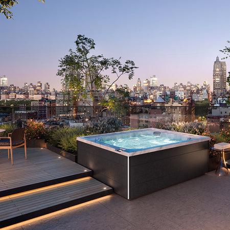 Jacuzzi J-LXL Deluxe Modell Whirlpool auf einer Dachterrasse mit Blick auf die Stadt bei Abenddämmerung.