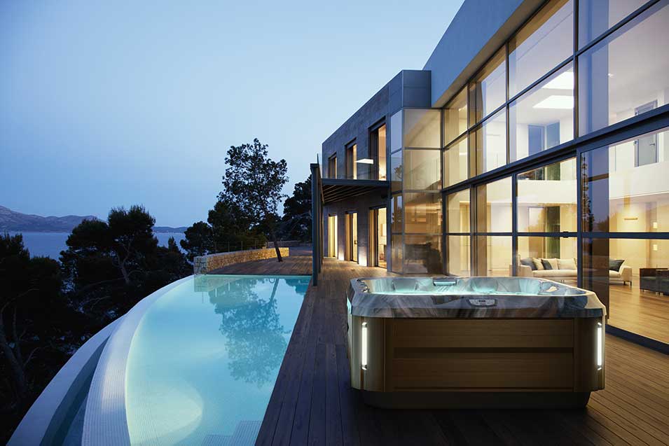 Jacuzzi Spa auf moderner Terrasse mit Infinity-Pool und beeindruckender Architektur im Hintergrund.