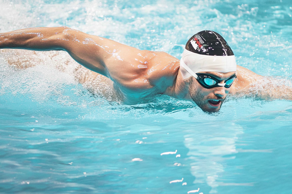 Sportlicher Schwimmer bei seinem intensiven Schwimmtraining im Swimmingpool gegen die Gegenstromanlage.