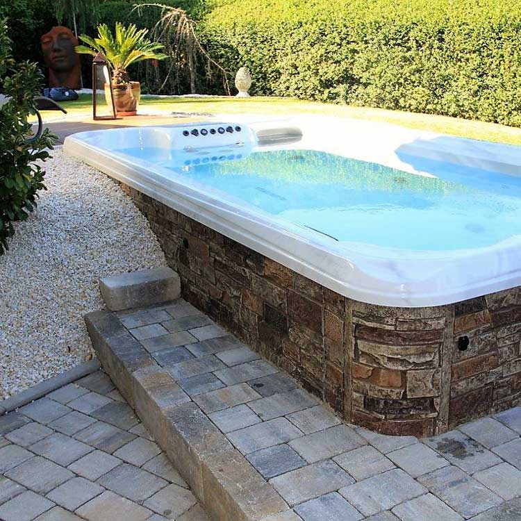 Semi-Inground Swim Spa, teilweise im Boden versenkt, mit Steinverkleidung im Garten.