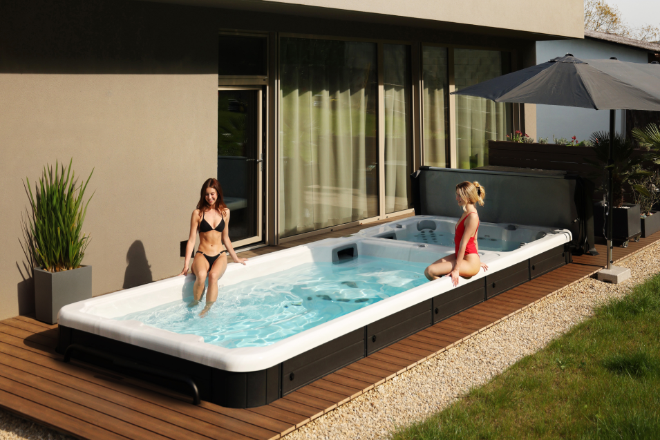 Zwei junge Frauen sitzen am Beckenrand eines Swimmingpools und genießen die Sonne am Pool.