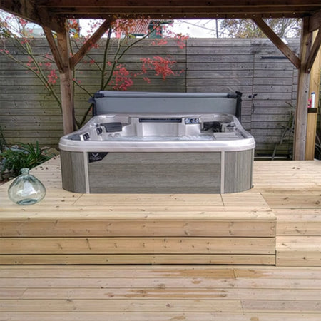 Whirlpool elegant in eine Holzterrasse integriert, umgeben von Pflanzen, Sichtschutzwand und stilvoller Außenbeleuchtung.